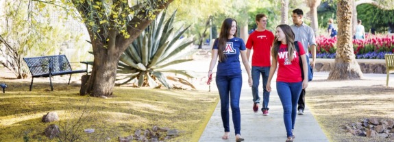 ɫӰ students walking on campus path near flowers and a shady tree